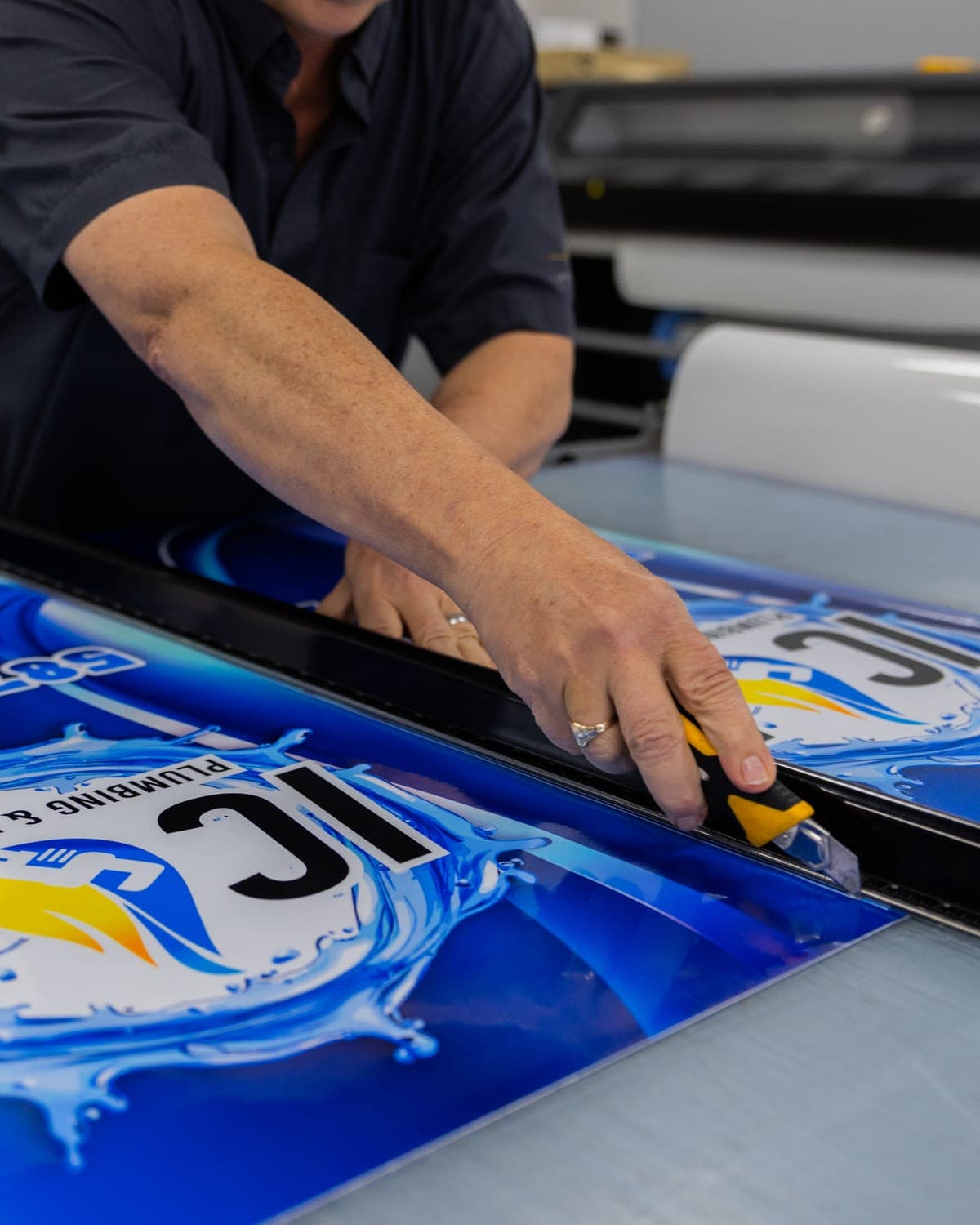 Trimming a printed ICON Plumbing vinyl panel on the cutting table